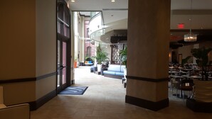 A hotel lobby with a central seating area, a staircase, and a dining area.