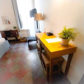 A small, bright room with a wooden table, a potted plant, a lamp, and a radiator.