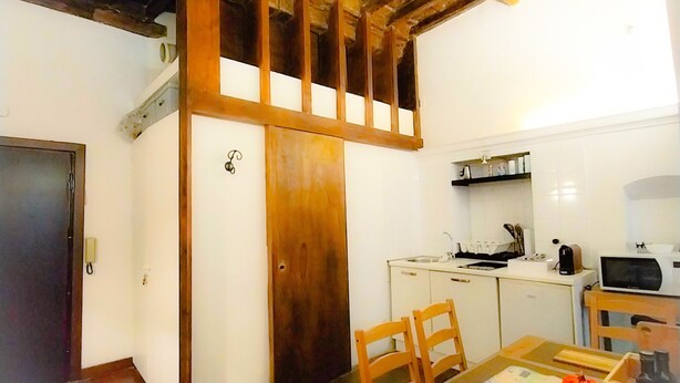 Une cuisine de taille réduite avec des meubles blancs, un plafond en bois et un coin repas comprenant une table et des chaises.