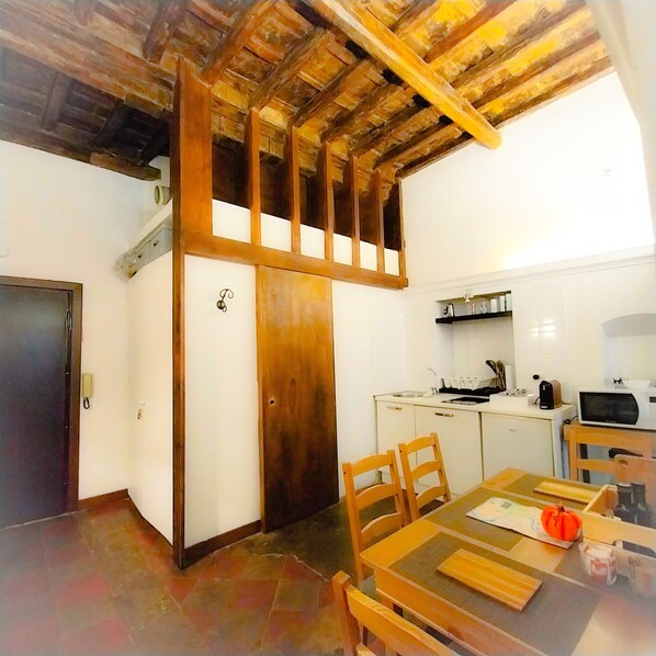 A compact kitchen with white cabinets, a wooden ceiling, and a dining area with a table and chairs. - Romantic apartment near St. Peter's (Roma)