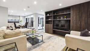 Een moderne woonkamer met een bank, fauteuil en salontafel. Er staat een televisie op een houten kast.