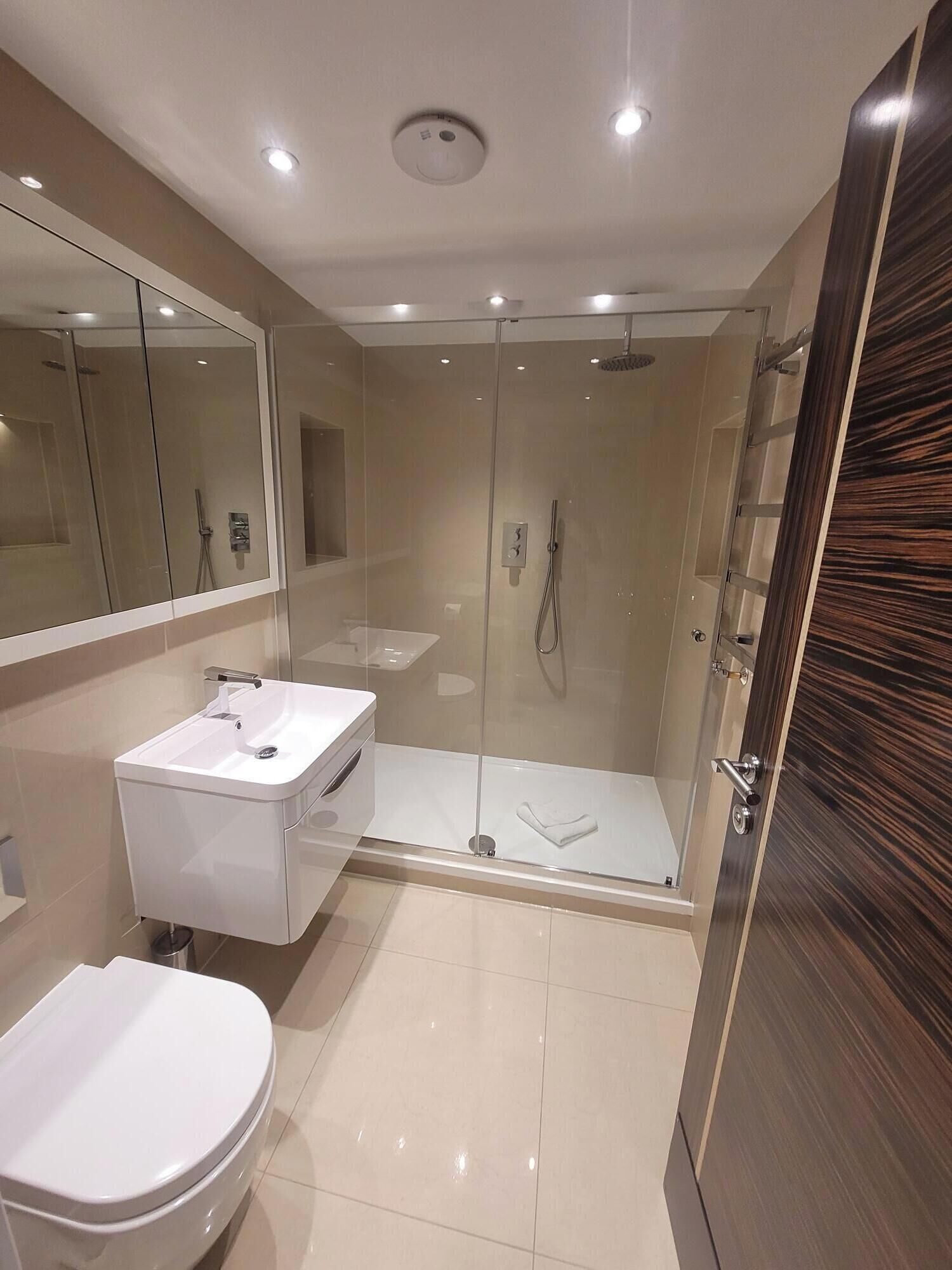 A modern bathroom with a glass-enclosed shower, a white sink, and a toilet.