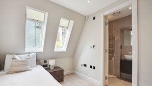 Een slaapkamer met een bed, nachtkastje, lamp en uitzicht op een badkamer door een geopende deur.