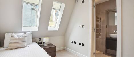 A bedroom with a bed, bedside table, lamp, and a view of a bathroom through an open door.