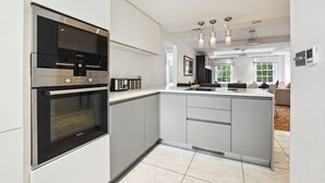 Een moderne keuken met een inbouwoven, een groot kookeiland met spoelbak en hangende lampen.