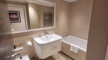 A modern bathroom with a sink, mirror, and bathtub.