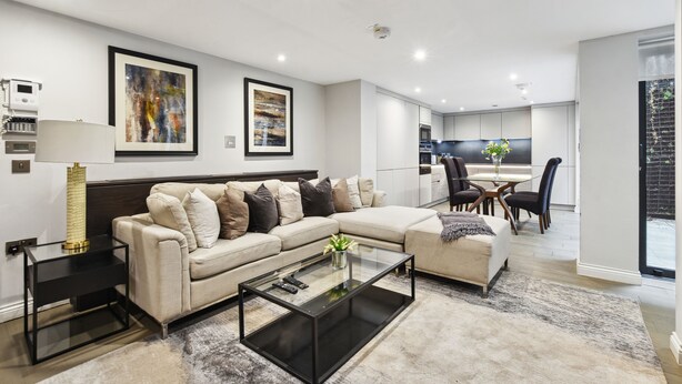 Een moderne woonkamer met een hoekbank, een glazen salontafel en een eethoek met een tafel en stoelen.