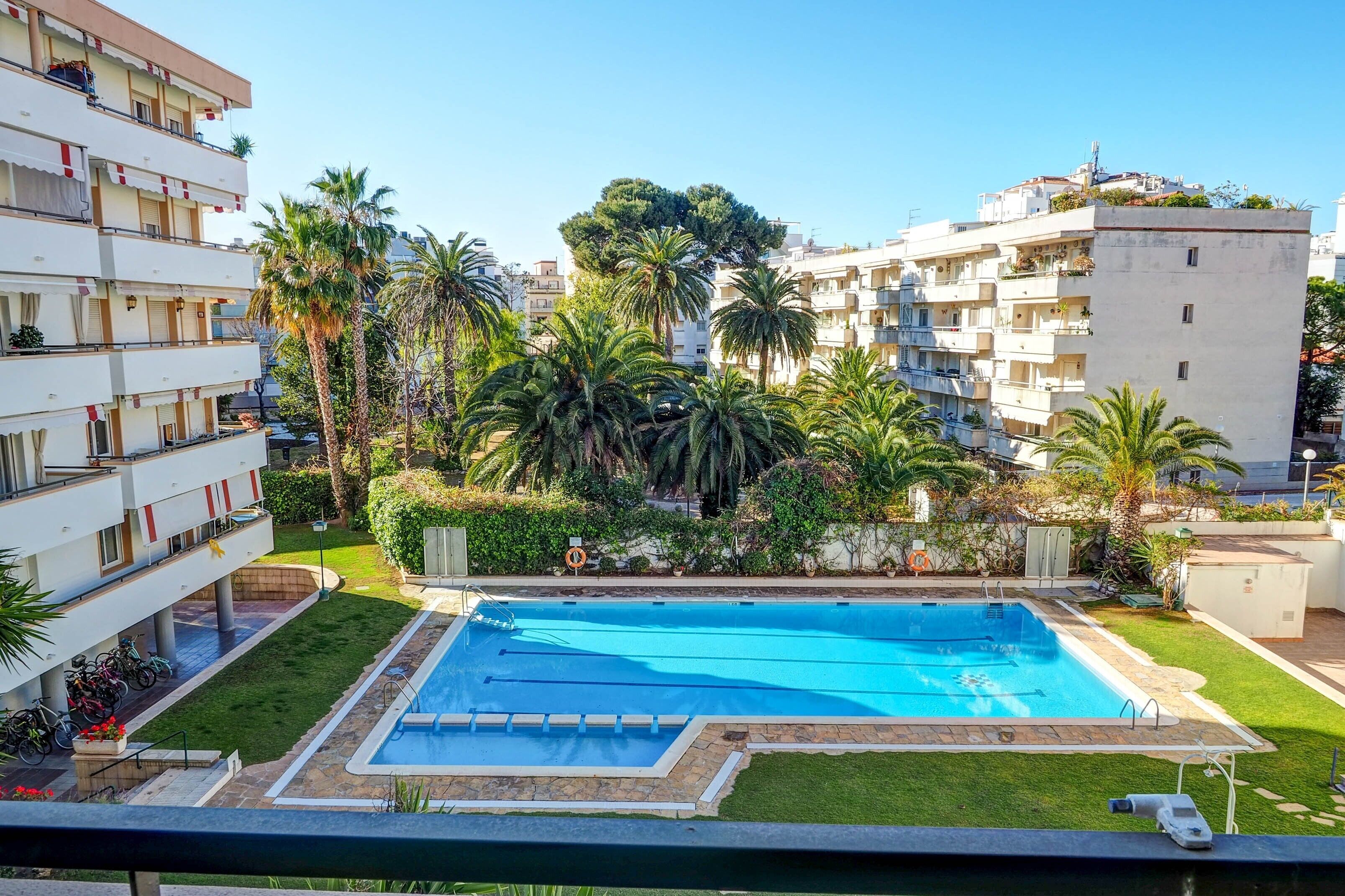 A swimming pool surrounded by palm trees and a multi-story building with balconies.