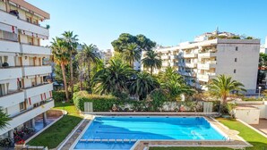 Ein Pool, umgeben von Palmen und ein mehrgeschossiges Gebäude mit Balkonen.