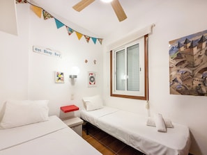 A room with two single beds, a red nightstand, a wall clock, and a window with a view of a castle.