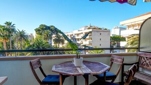 Ein Balkon mit Holztisch und -stühlen, einem Blumentopf und Blick auf Gebäude und Palmen.