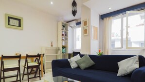 A living room with a dark blue sofa, two wooden chairs, a glass coffee table, and a small table with a yellow tray. - Sunflower Apartment by Hello Homes Sitges (Sitges)