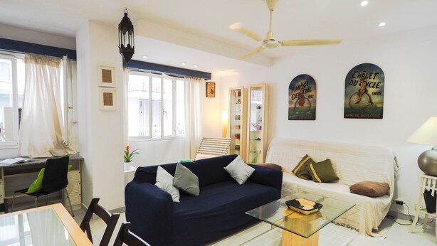 A living room with a dark blue sofa, a glass coffee table, and a ceiling fan. - Sunflower Apartment by Hello Homes Sitges (Sitges)