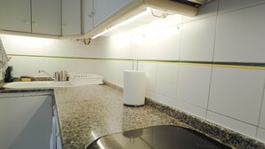 A kitchen with white cabinets, a granite countertop, a stainless steel sink, and a white trash bin. - Sunflower Apartment by Hello Homes Sitges (Sitges)