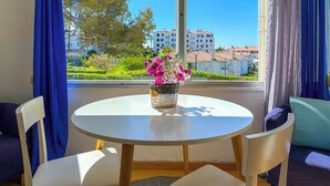 A round table with a vase of flowers, two white chairs, and a view of buildings and greenery through large windows. - The Blue Island Loft by Hello Homes Sitges (Sitges)