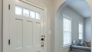 A hallway with a white door, wooden flooring, and a seating area with a grey sofa and pillows. - Chevy Chase-1mi to Rupp-Kroger Field-Downtown (Lexington)