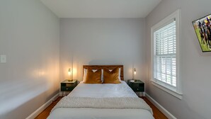 A bedroom with a large bed, two bedside tables, a window with blinds, and a wall-mounted TV. - Chevy Chase-1mi to Rupp-Kroger Field-Downtown (Lexington)