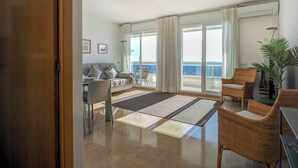Un amplio salón con balcón, un sofá, una mesa de comedor y sillas de mimbre.