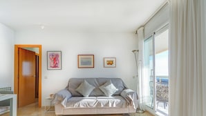 Una sala de estar moderna con un sofá gris, dos cojines, una mesita auxiliar y una lámpara de pie. Hay tres obras de arte enmarcadas en la pared y una puerta de madera que da a otra habitación.