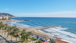 Vista costera con playa, palmeras y un rompeolas rocoso.
