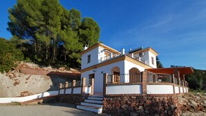 Une maison à deux étages, avec des fondations en pierre, une façade blanche et un balcon.