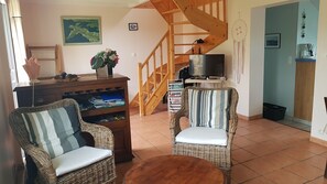 Un salon avec des meubles en osier, un escalier en bois, une télévision et une machine à café.