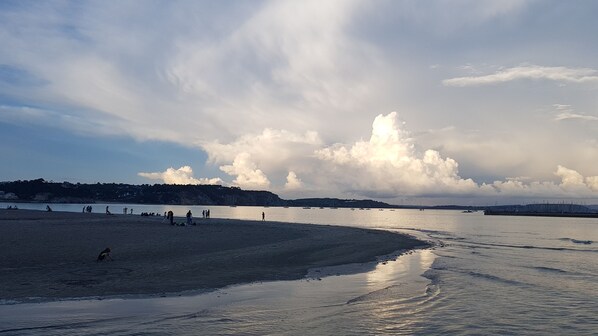 Une plage avec des gens et des bateaux, une mer calme et un ciel nuageux.