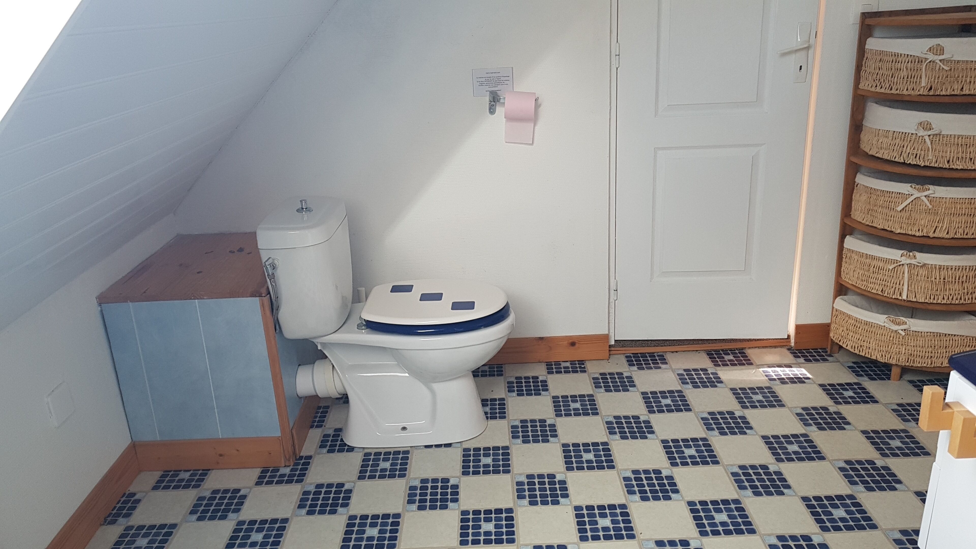 A small bathroom with a toilet, a shelf with baskets, and a tiled floor.