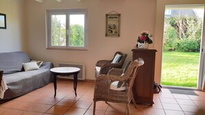 Un salon avec un canapé gris, deux fauteuils en osier, une petite table ronde et un meuble sur lequel est posé un vase de fleurs.
