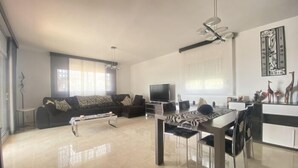 A modern living room with a sofa, a coffee table, a TV, and a dining area with chairs and a table.