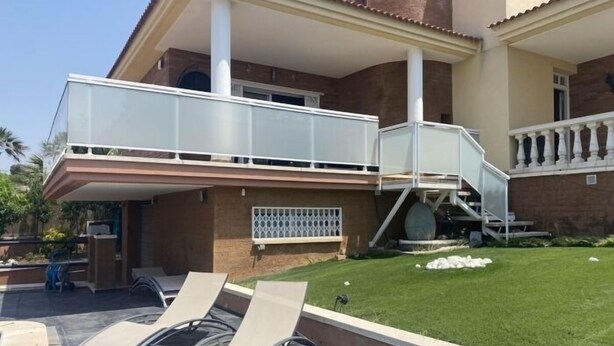 A two-story house with a balcony, a covered outdoor seating area, and a well-maintained lawn.