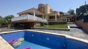 A residential building with a swimming pool, a covered patio, and a well-maintained lawn.