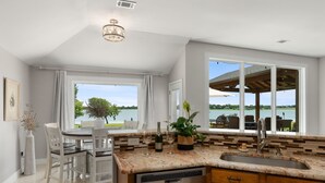 A modern kitchen with a view of a lake, a dining area with a table and chairs, and a built-in dishwasher.