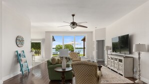 A spacious living room with a large window, a ceiling fan, a television, and a fireplace.