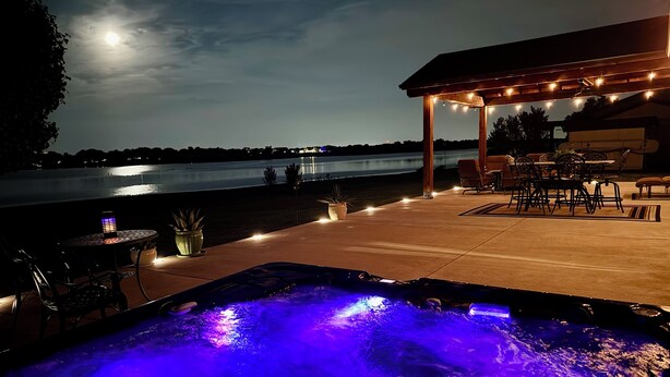 A hot tub with blue lighting, outdoor seating, and a view of a lake at night.