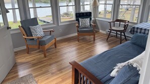 A room with large windows, wooden flooring, a blue sofa, and two wooden chairs.