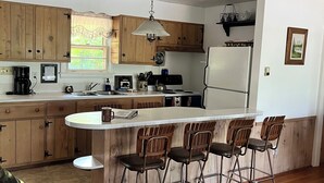 A modern kitchen with wooden cabinets, a central island with bar stools, a hanging light fixture, and a refrigerator.