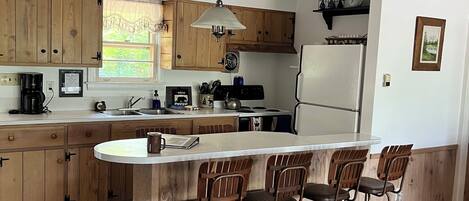 Una cocina moderna con armarios de madera, una isla central con taburetes de bar, una lámpara colgante y un refrigerador.