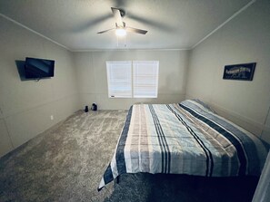 Quarto com cama, ventilador de teto, televisão e janela com persianas.