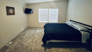 Un dormitorio con cama, ventilador de techo, televisor montado en la pared y ventana con persianas.