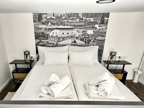 A modern hotel room with a large bed, two bedside tables, and a cityscape tapestry on the wall.