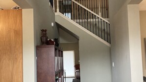 Ein großzügiger Innenraum mit einer Holzbücherwand, einer Treppe zu einer oberen Ebene und Blick auf einen Wohnbereich.