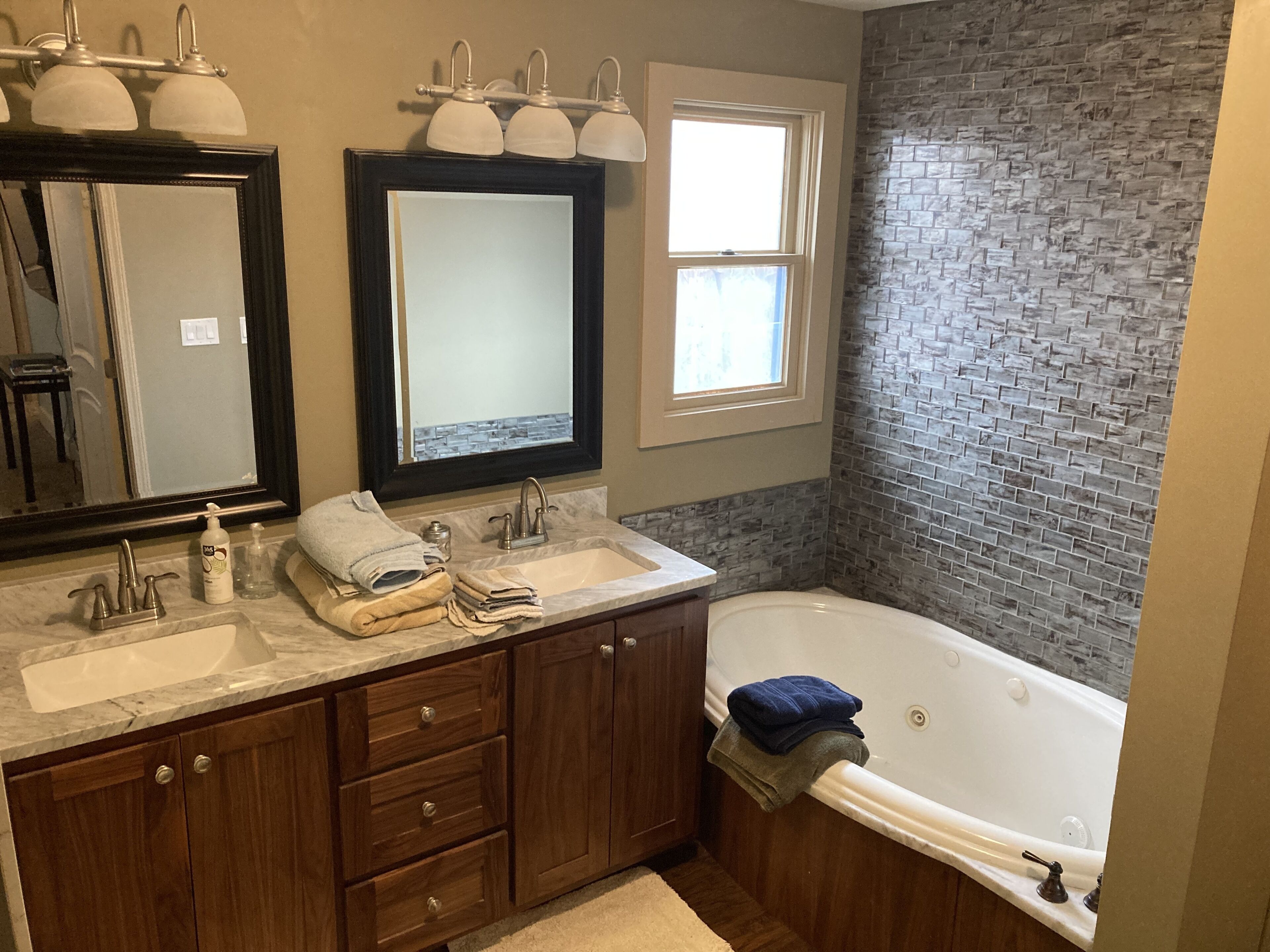 A bathroom with a large mirror, two sinks, a bathtub, and a window.