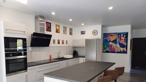 Uma cozinha moderna com ilha central, banquetas e um quadro abstrato colorido na parede.