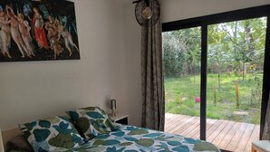 Quarto com cama, um quadro, uma luminária e vista do jardim através de uma porta deslizante.