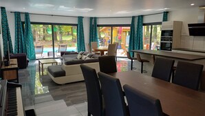 Uma sala de estar moderna com sofá, mesa de jantar, cadeiras, um piano e vista para uma área de piscina externa.