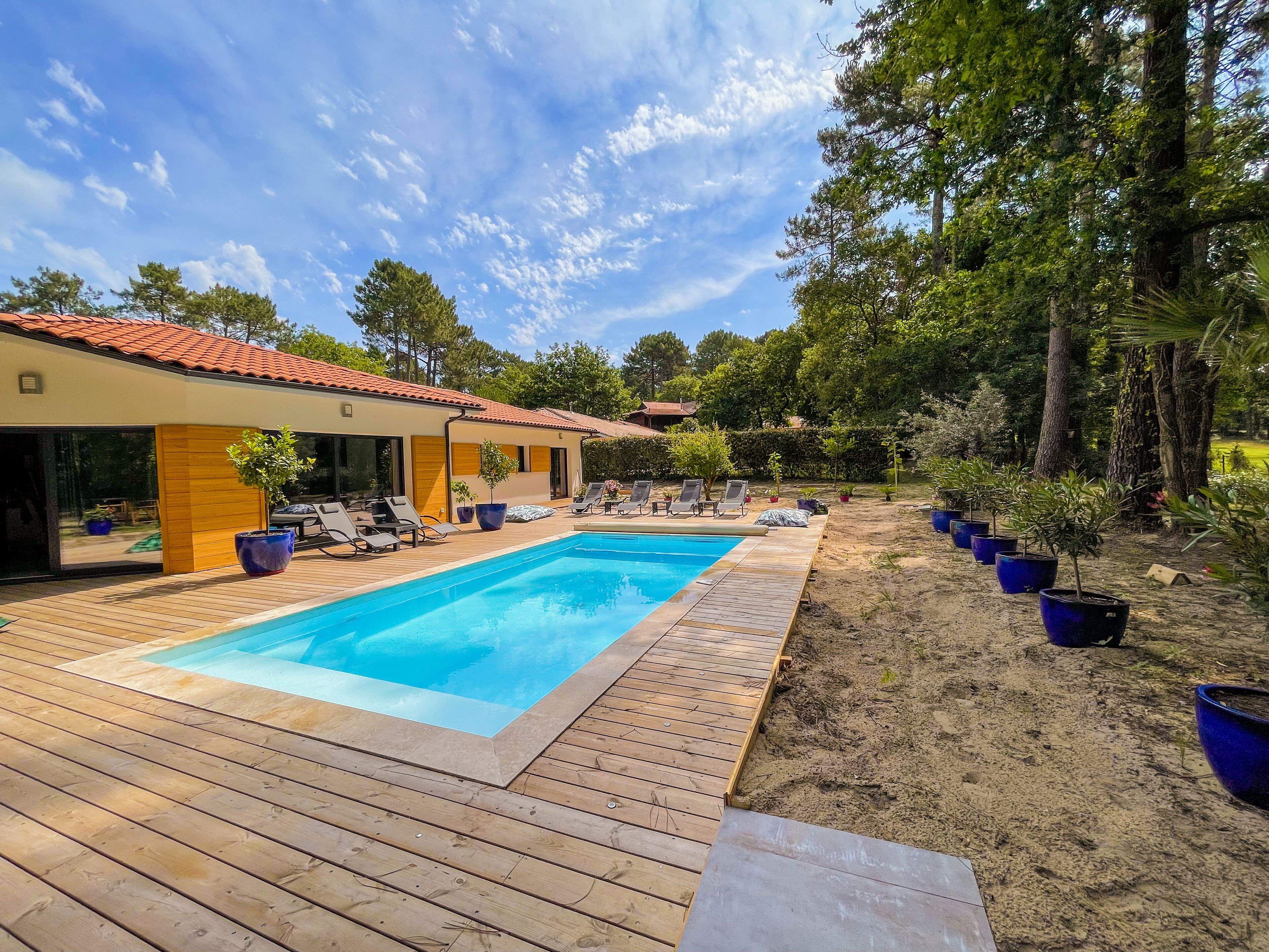 Ein Schwimmbecken mit Holzterrasse, Liegestühlen und Topfpflanzen.