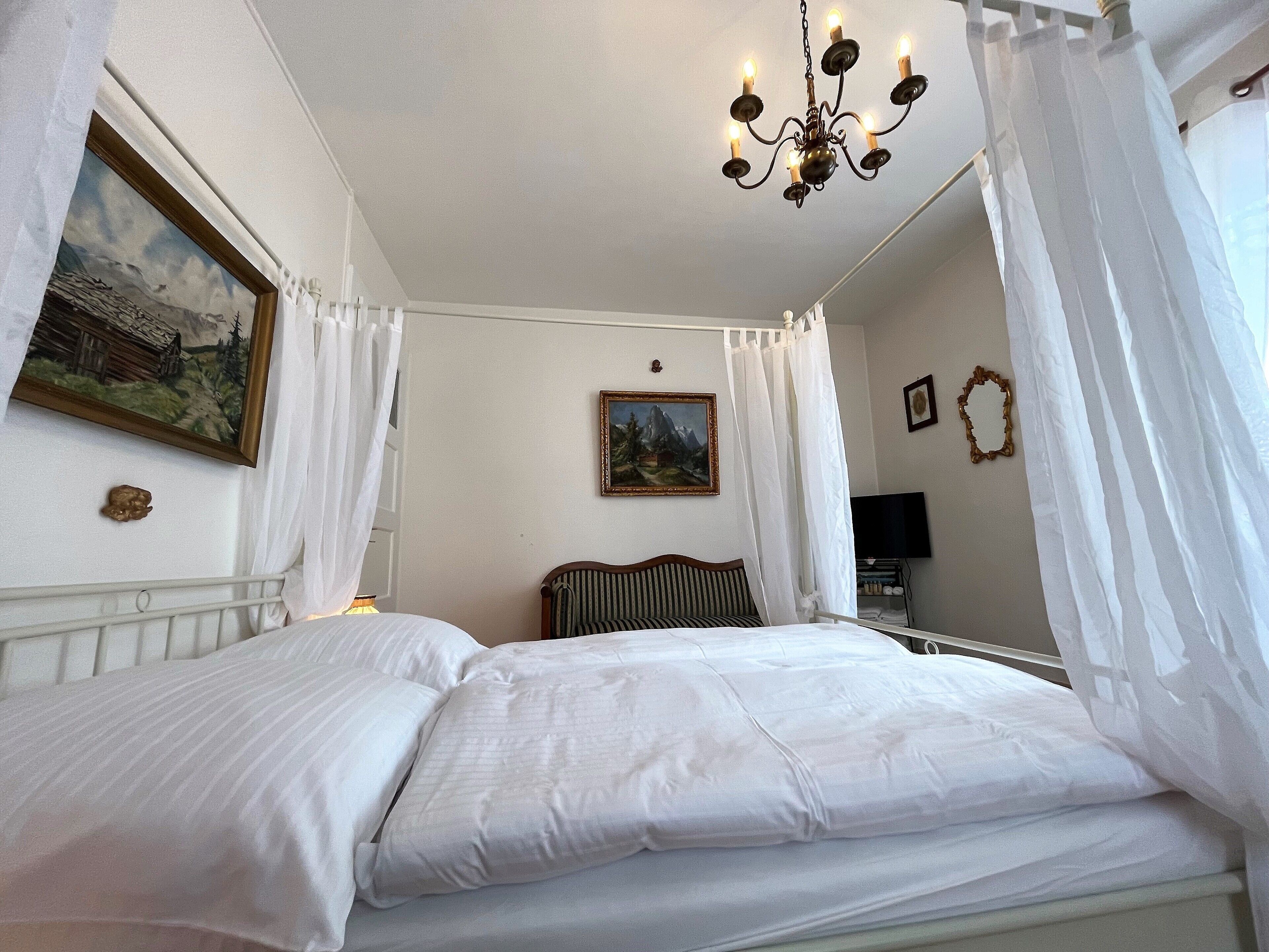 Une chambre à coucher avec un lit, un lustre, un tableau et un miroir.