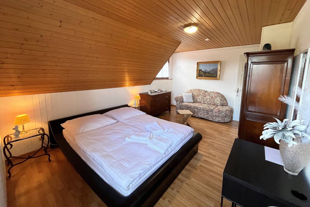 A bedroom with a wooden ceiling, a bed, a nightstand, a chair, a wardrobe, and a painting on the wall.
