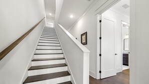 Een trap met witte muren en donkere houten treden die leidt naar een kamer met een witte deur en een ingelijst kunstwerk aan de muur.